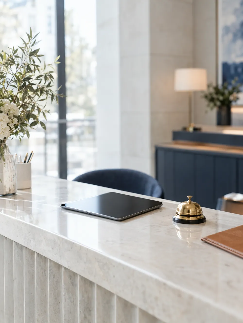Pale stone hotel reception desk with a tablet and a brass bell